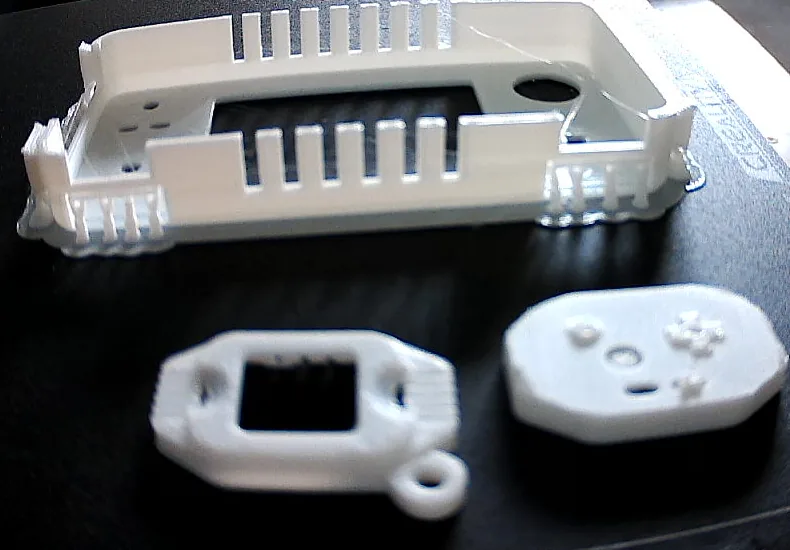 The first test prints on the printer bed, with the keychain's front and back in front of a larger handheld shell